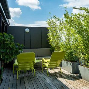 Loungebereich auf einer Dachterrasse mit Bambuspflanzen in Reinzinkgefäßen und grünen Stühlen