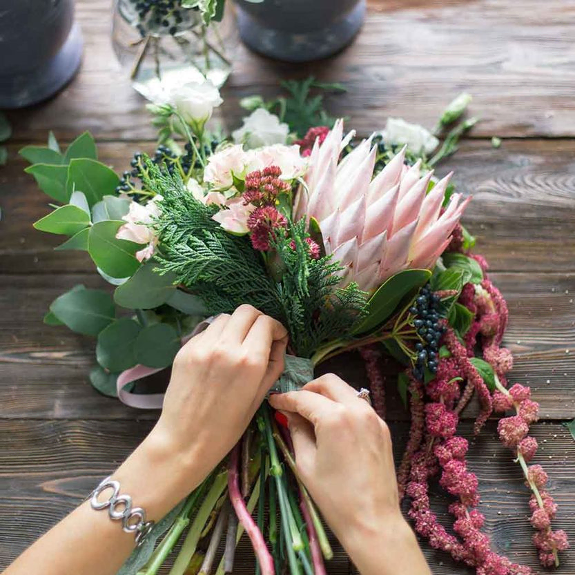 Floristin bei der Arbeit: Hübsche junge Frau stellt einen modischen, modernen Blumenstrauß aus verschiedenen Blumen her