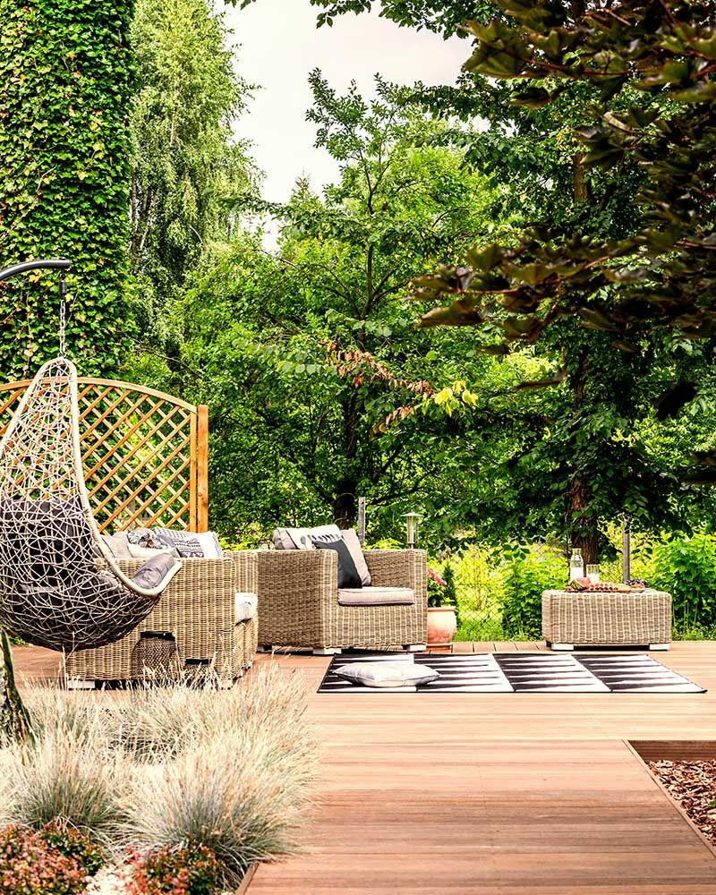 Hängesessel und Gartenmöbel auf der Terrasse in der Nähe von Bäumen im Sommer