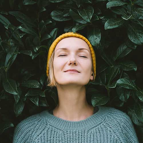Porträt einer entspannten und selbstbewussten Frau mit geschlossenen Augen vor dem Hintergrund einer grünen Blätterwand